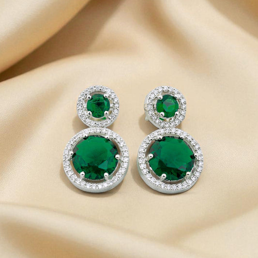 Pair of emerald green earrings on a beige fabric background