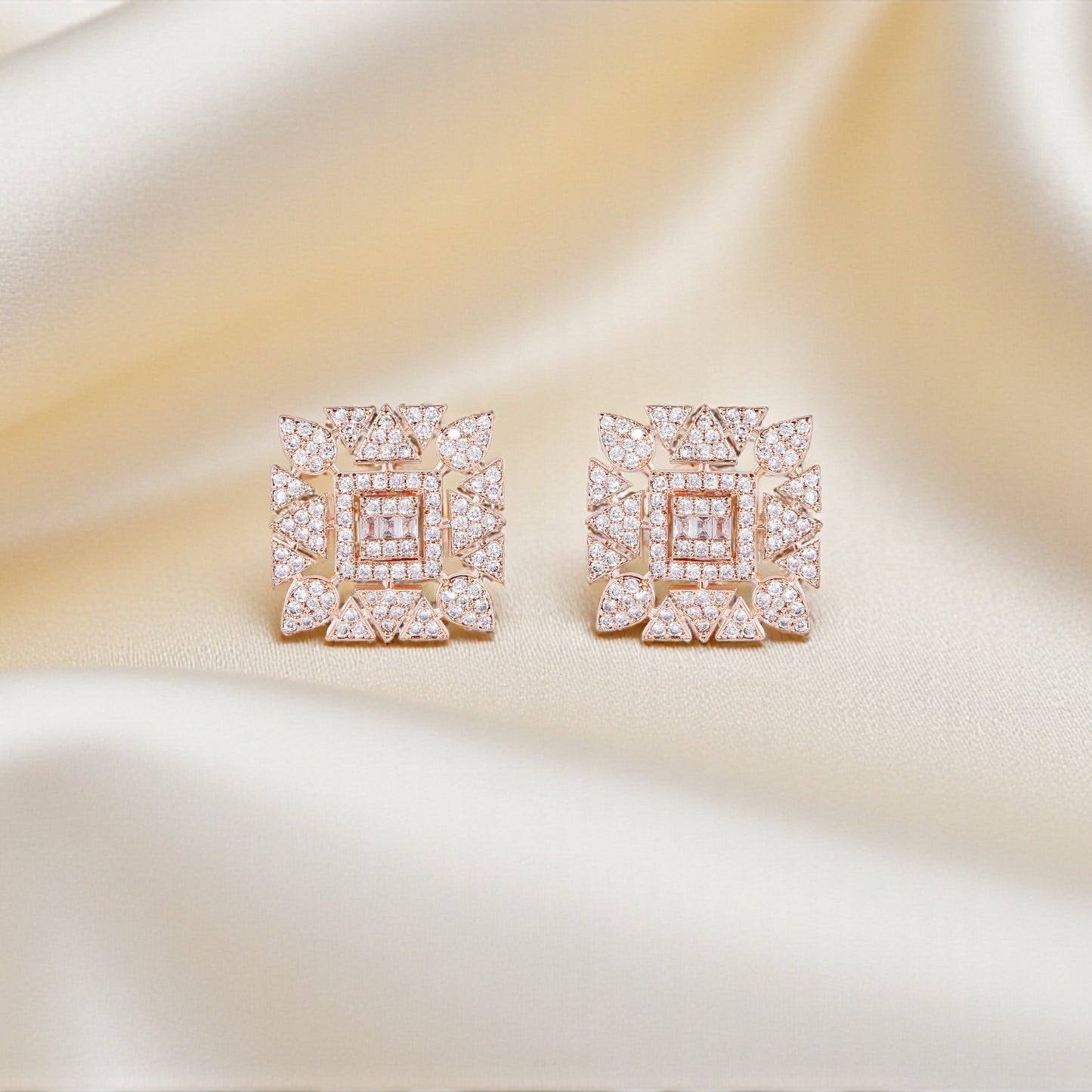 Pair of square-shaped earrings with pink gemstones on a satin surface