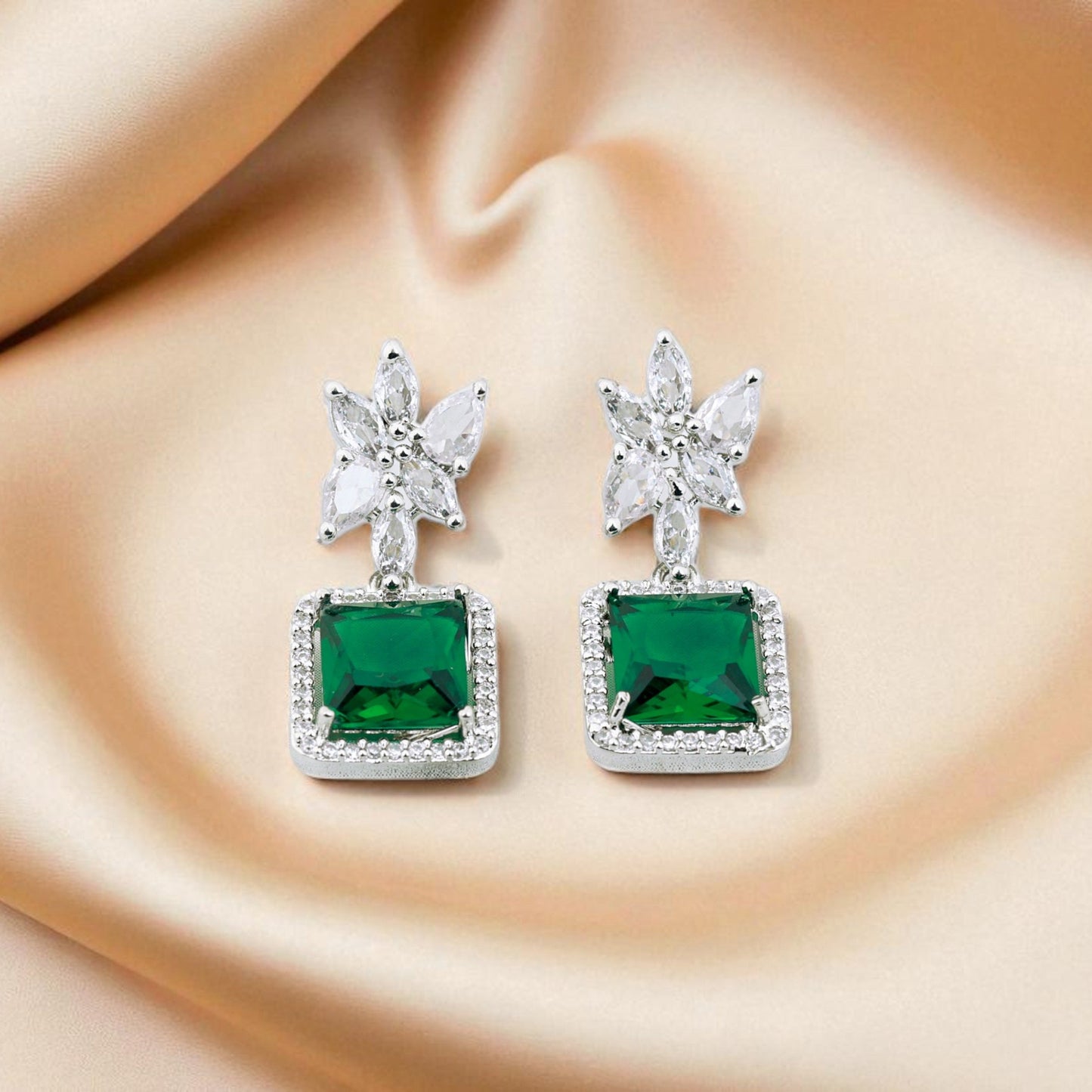 Green gemstone earrings with silver accents on a beige fabric background