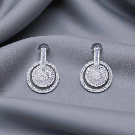 Pair of silver earrings with circular designs on a gray fabric background