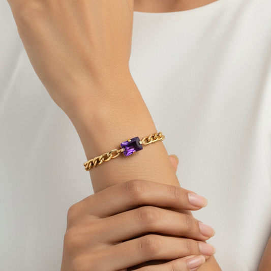 Gold bracelet with a purple gemstone on a model's wrist against a neutral background