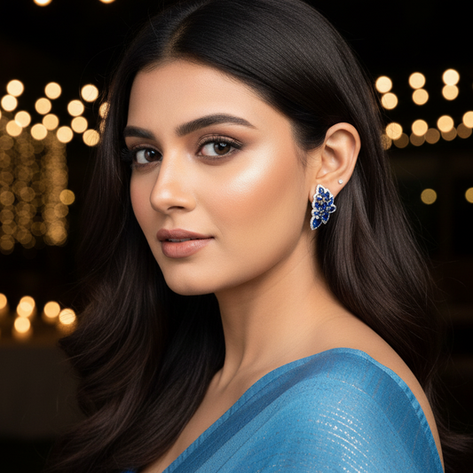 Woman wearing a blue saree with decorative earrings against a blurred lights background