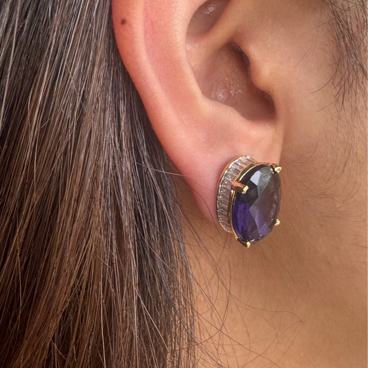 Close-up of an ear wearing a decorative earring with a purple gemstone.
