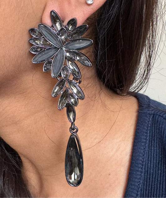 Close-up of a person wearing a silver floral earring with a teardrop pendant.
