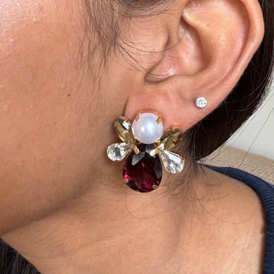 Close-up of an ear wearing a decorative earring with a red gemstone.