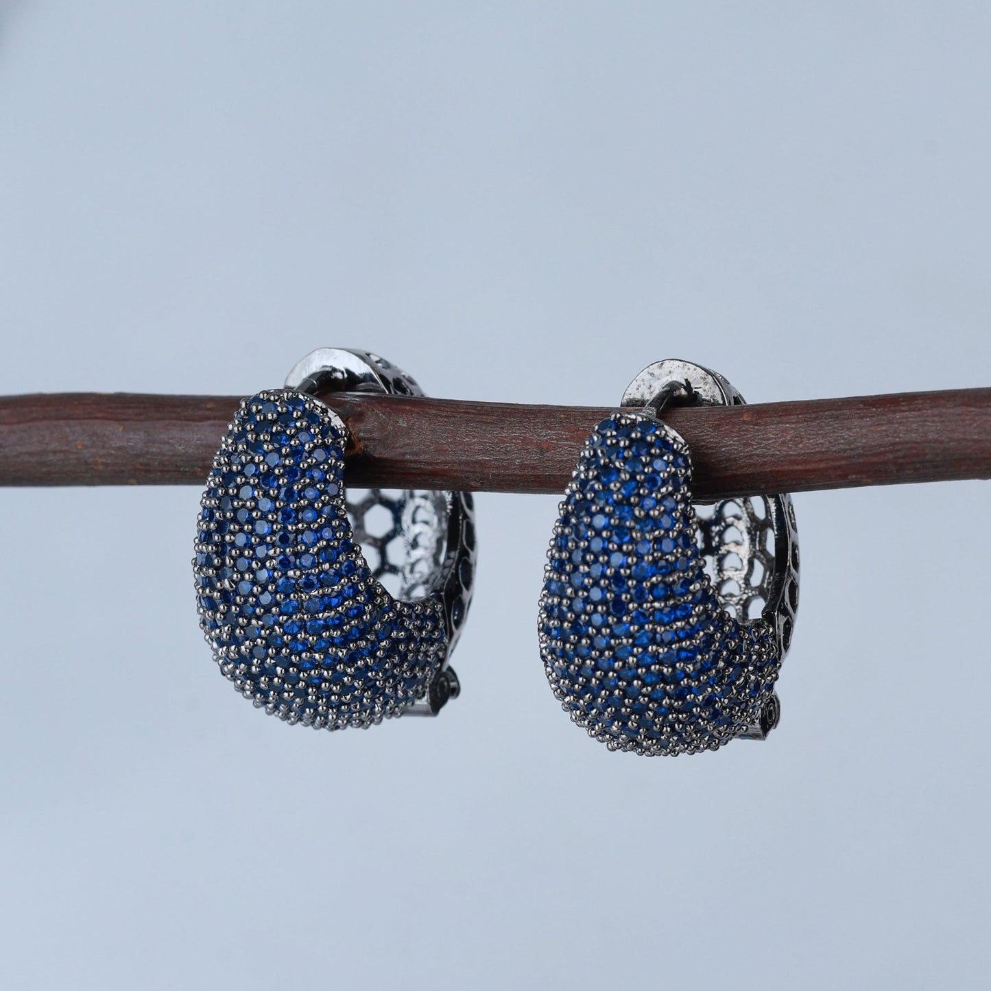 Pair of blue gemstone hoop earrings on a branch with a blurred background
