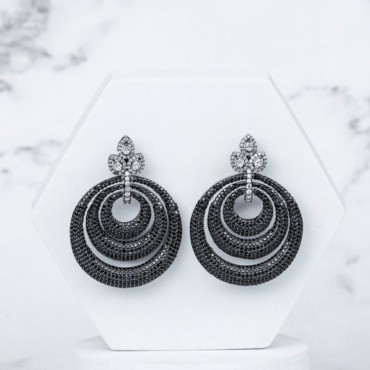 Pair of black hoop earrings on a white stand with a marble background