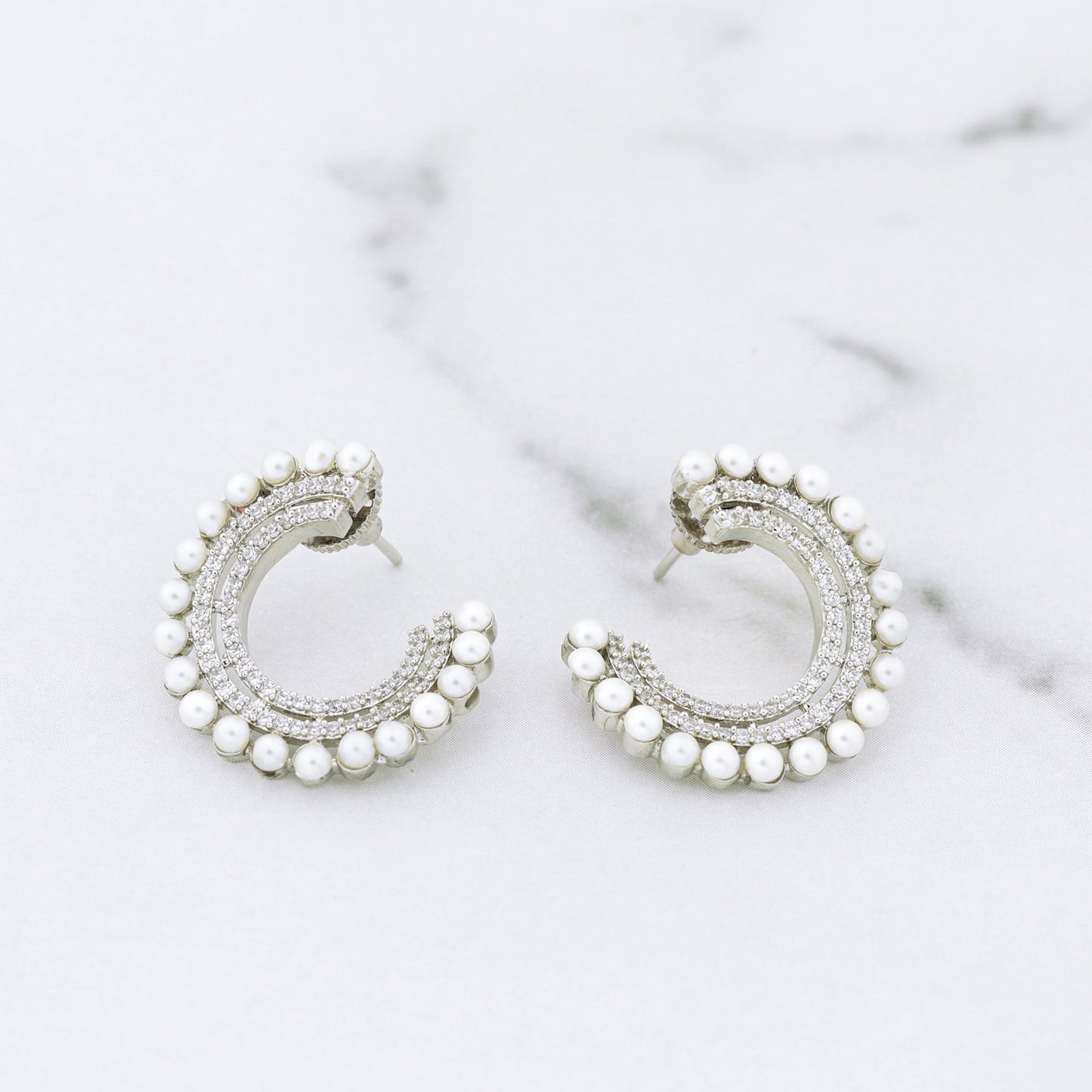 Silver hoop diamond earrings with pearl accents on a marble surface