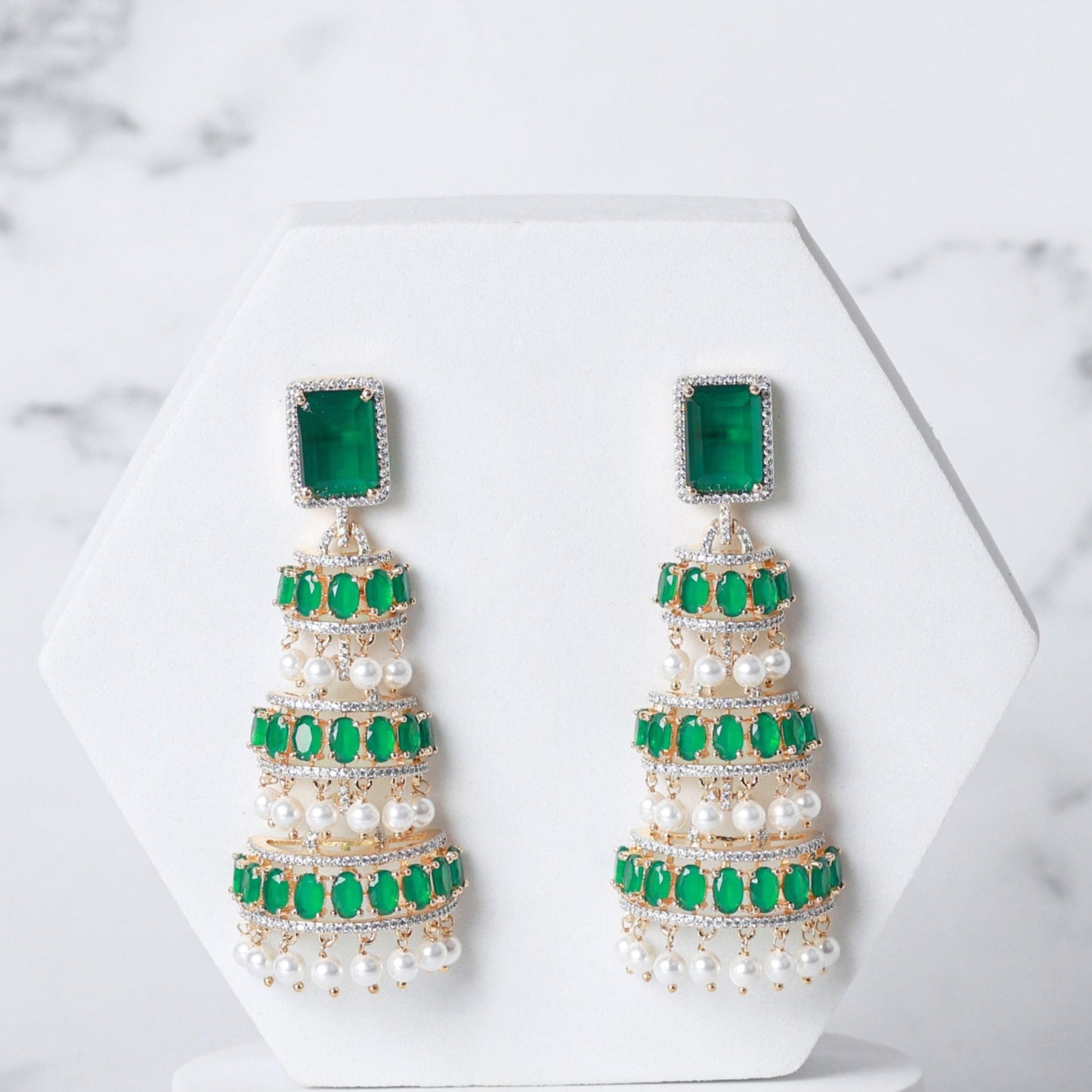 Pair of pearl earrings with green accents on a white marble background