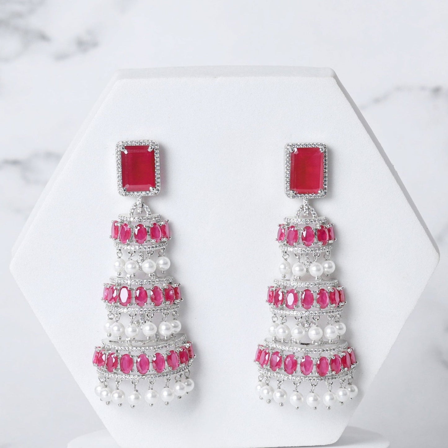 Pair of earrings with red and white stones on a marble background