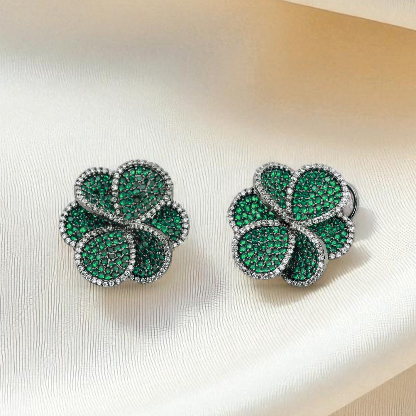Pair of green clover-shaped earrings on a soft fabric background