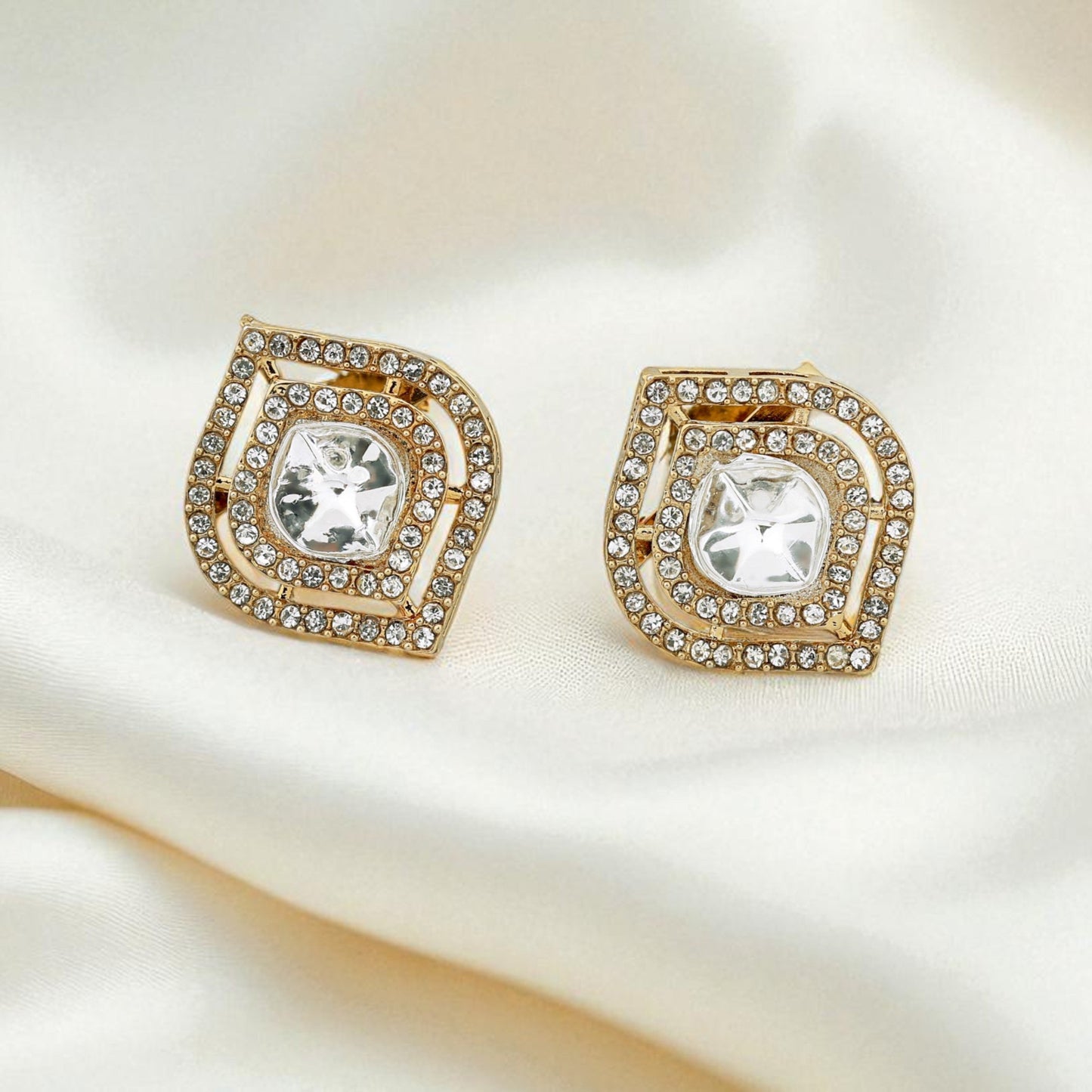 Gold earrings with clear gemstones on a white fabric background