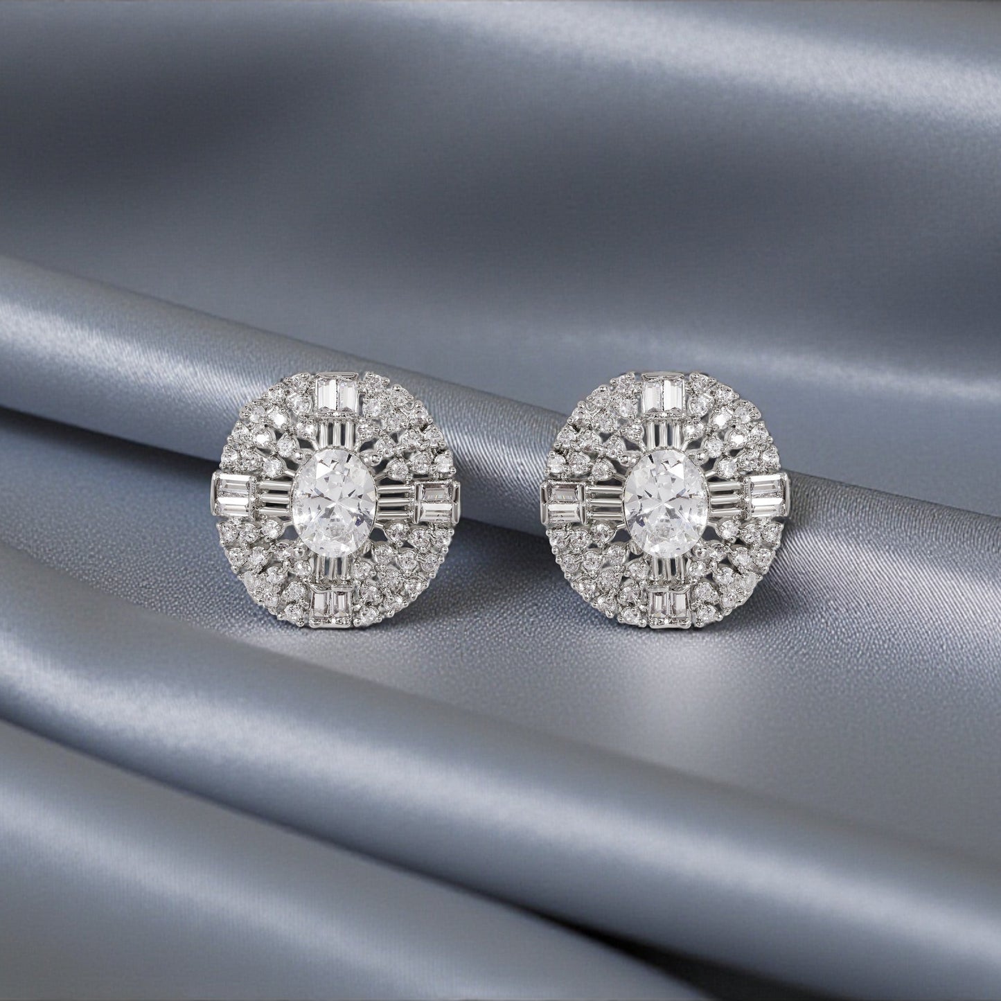 Pair of silver earrings with clear gemstones on a gray fabric background