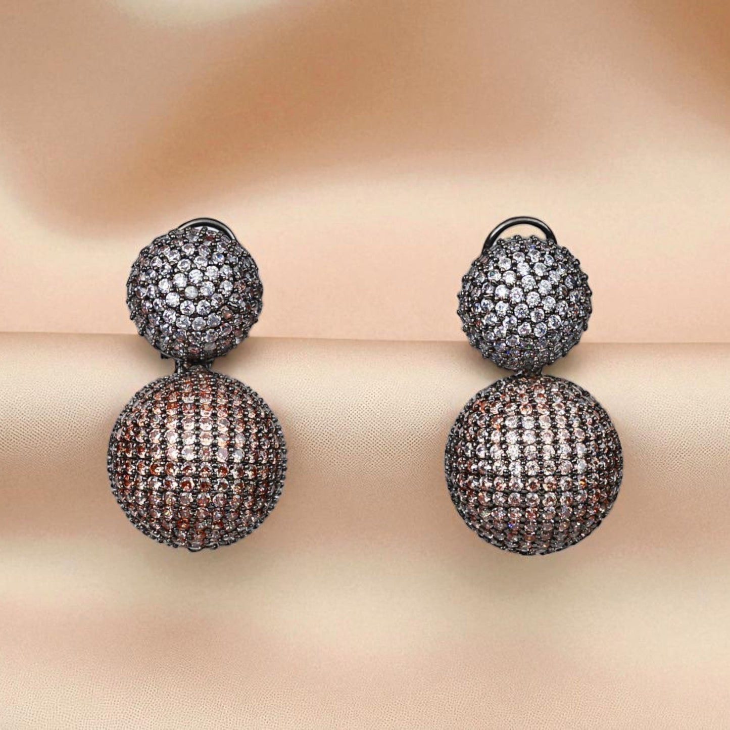 Pair of double-ball earrings with intricate detailing on a soft beige background