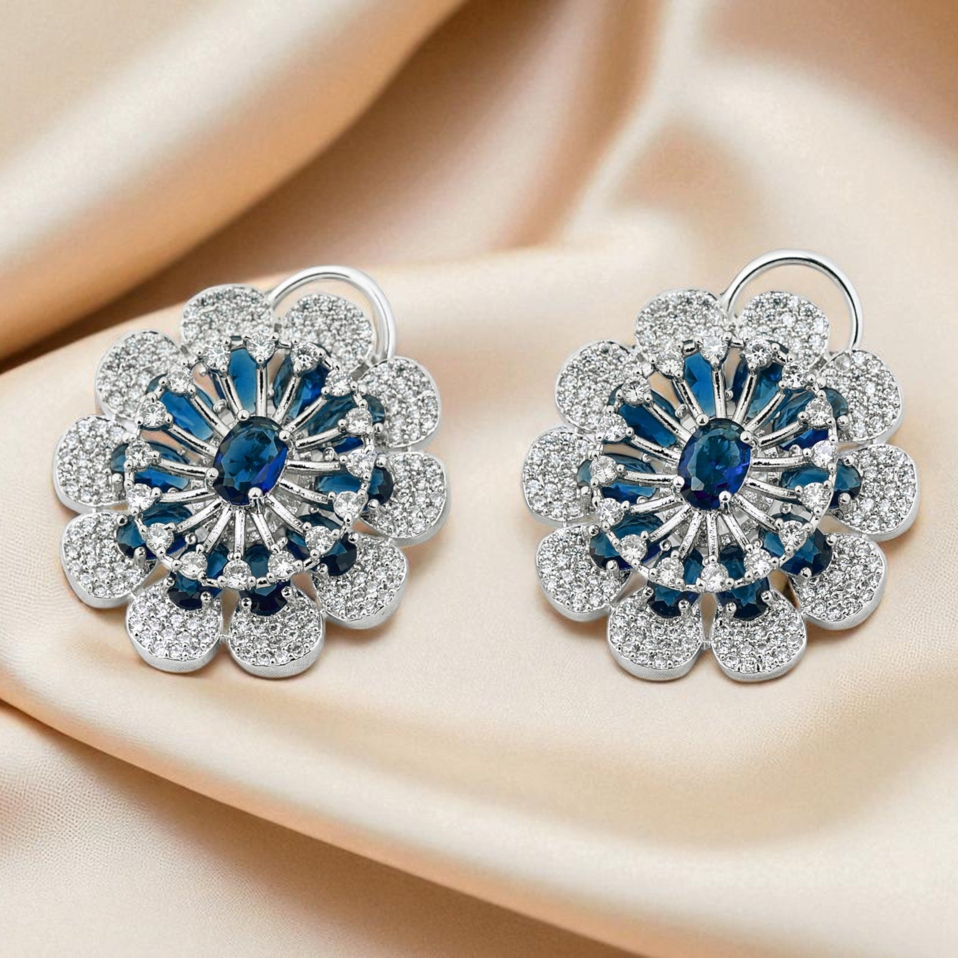 Pair of floral earrings with blue gemstones on a beige fabric background