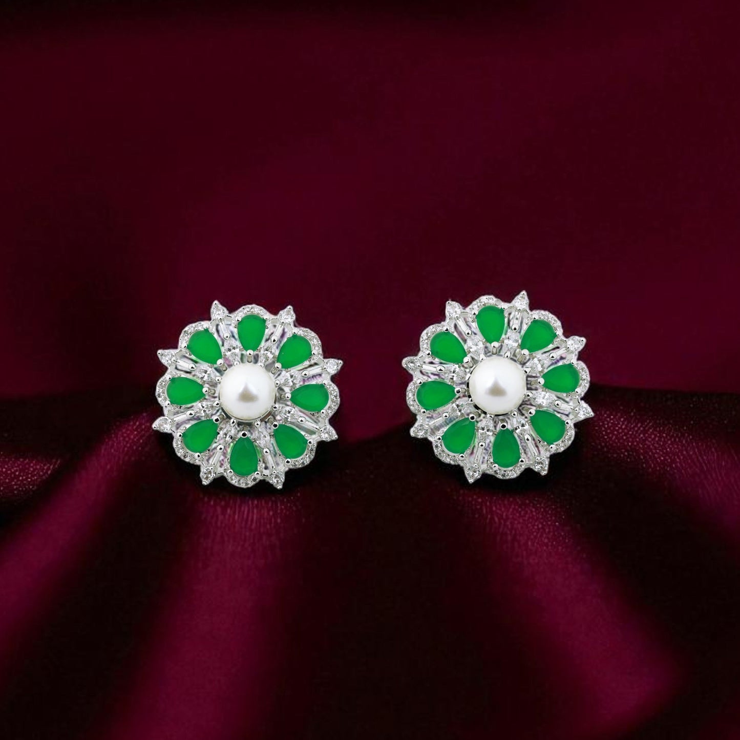 Pair of floral earrings with green and white stones on a burgundy fabric background