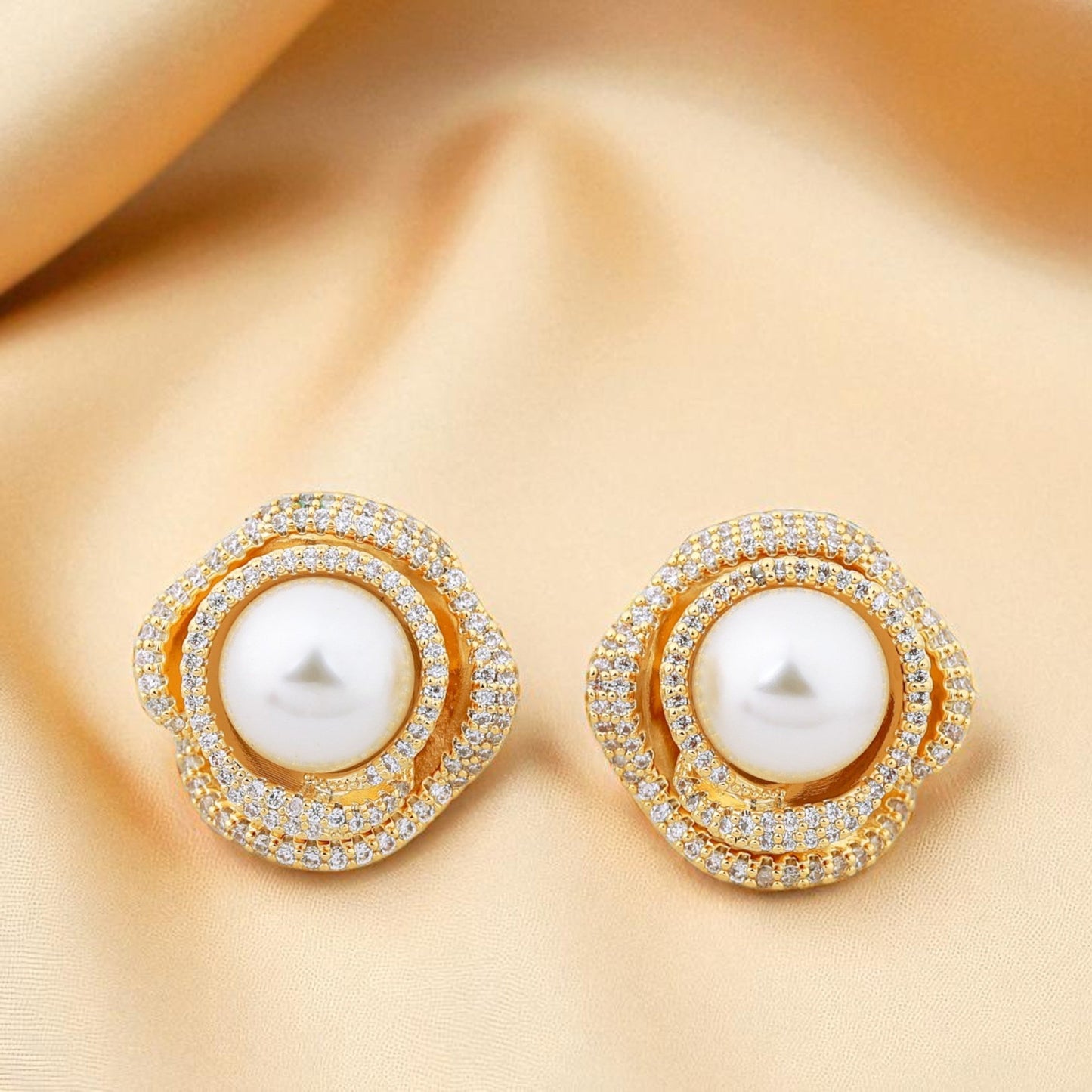 Pair of gold earrings with pearls on a beige fabric background