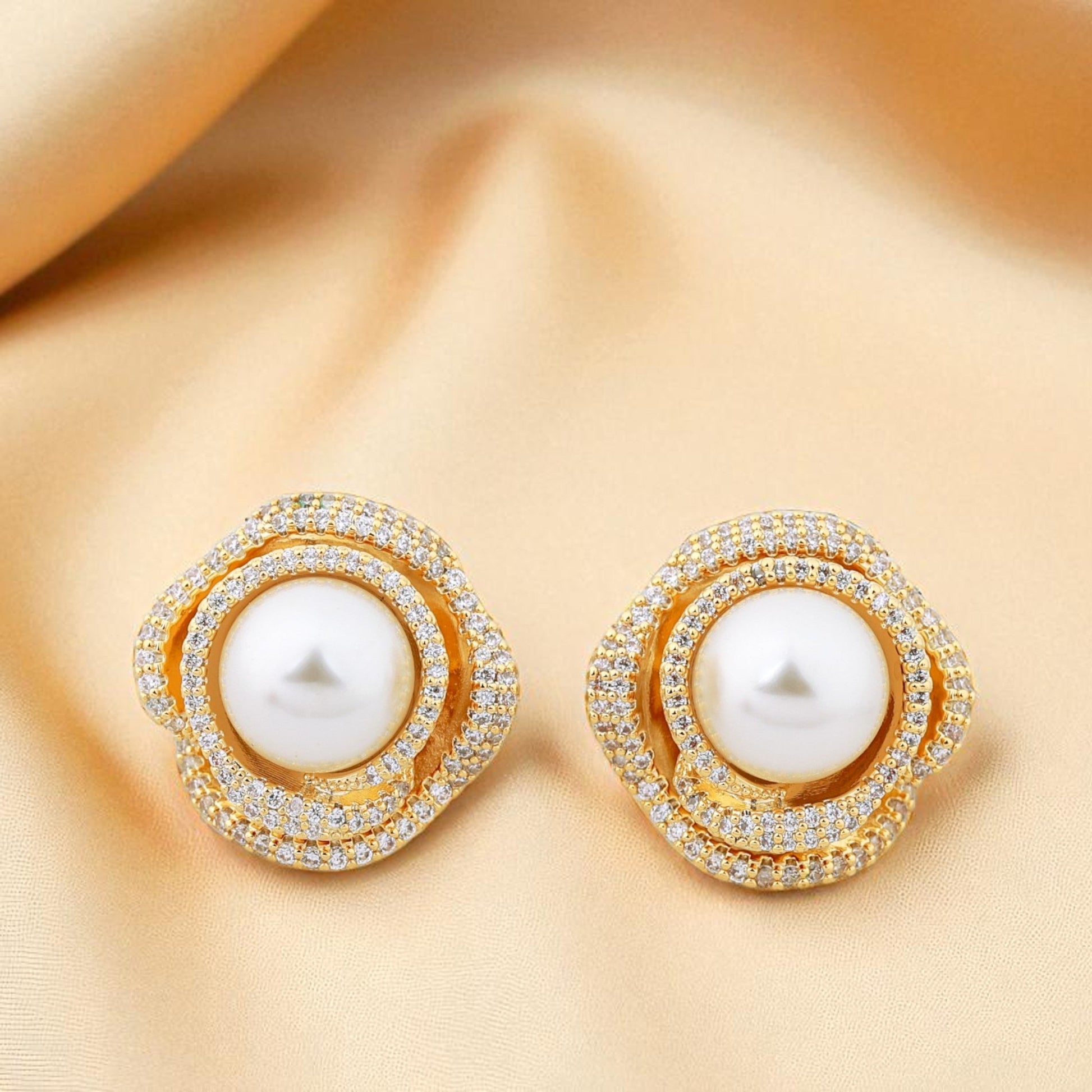 Pair of gold earrings with pearls on a beige fabric background