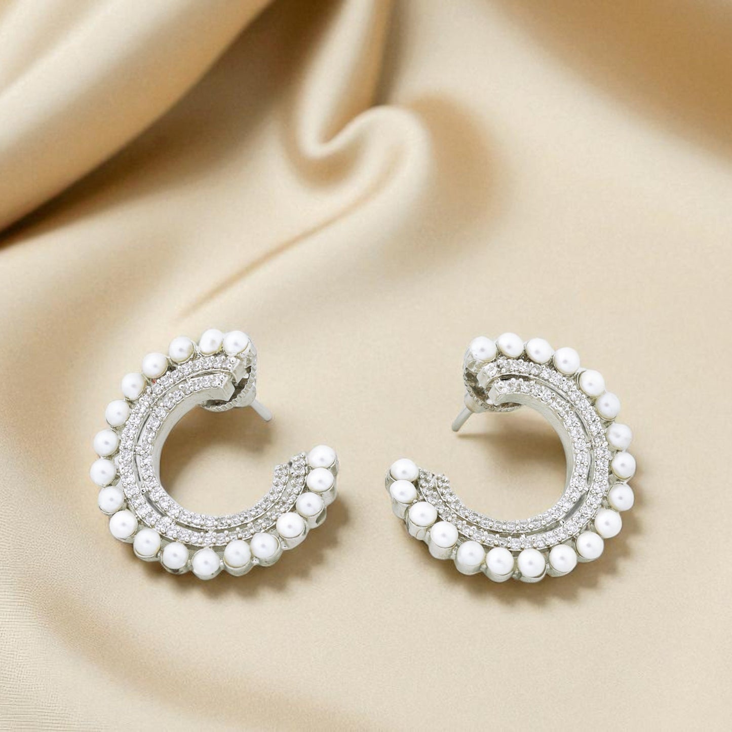 Pair of pearl and silver hoop earrings on a beige fabric background