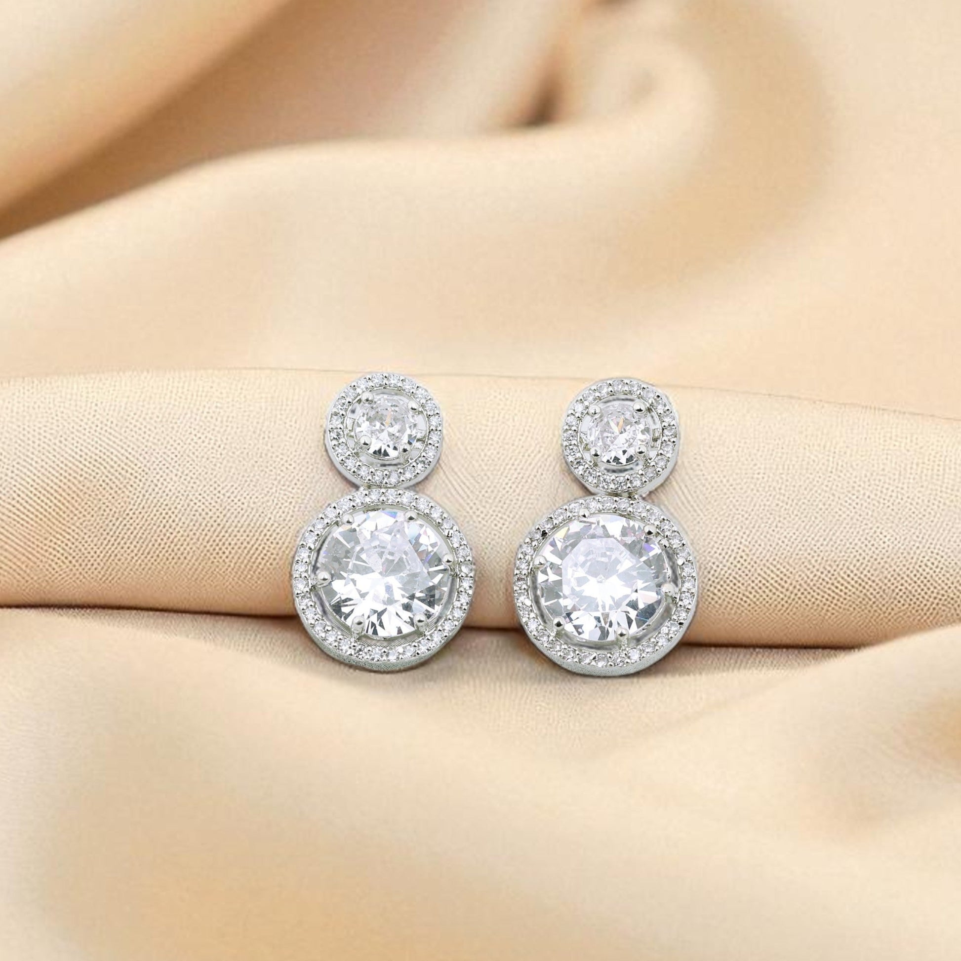 Silver earrings with clear gemstones on a beige fabric background