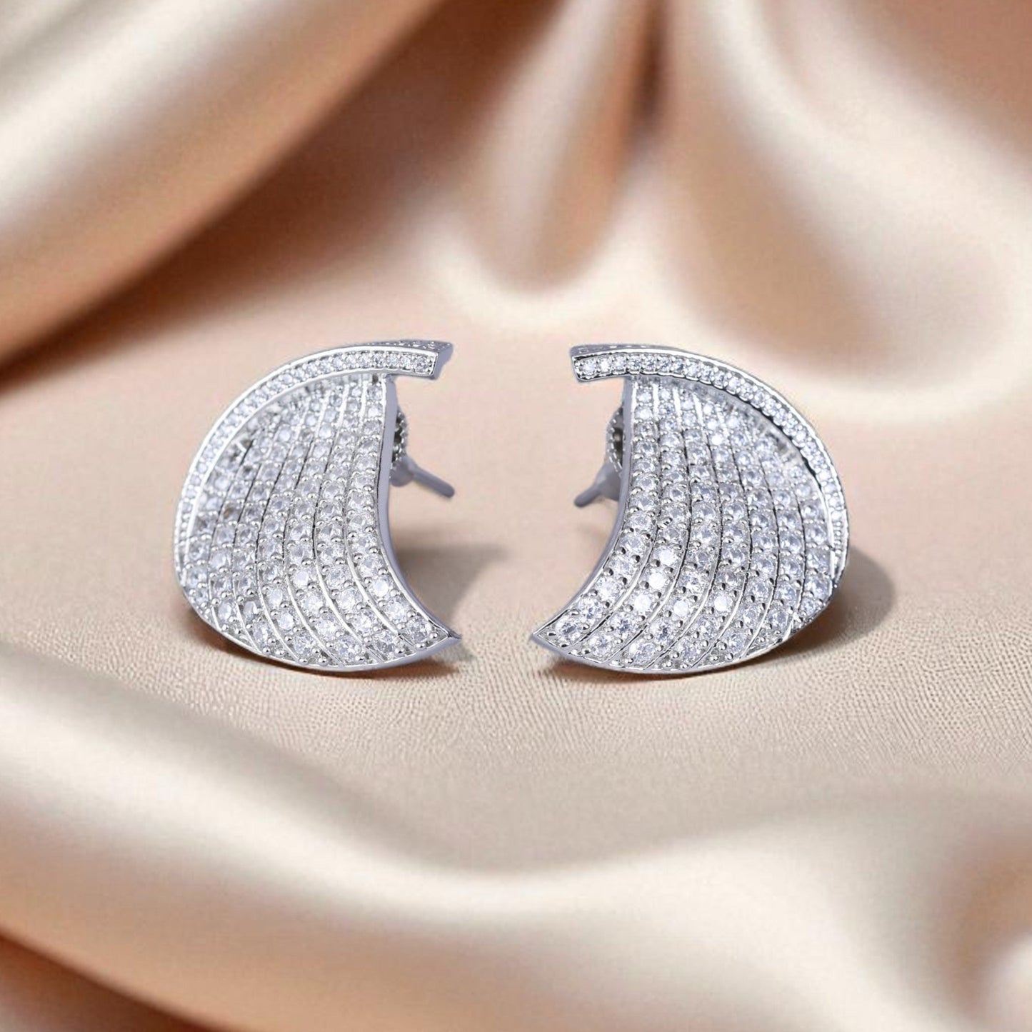 Silver crescent moon earrings on a beige satin background