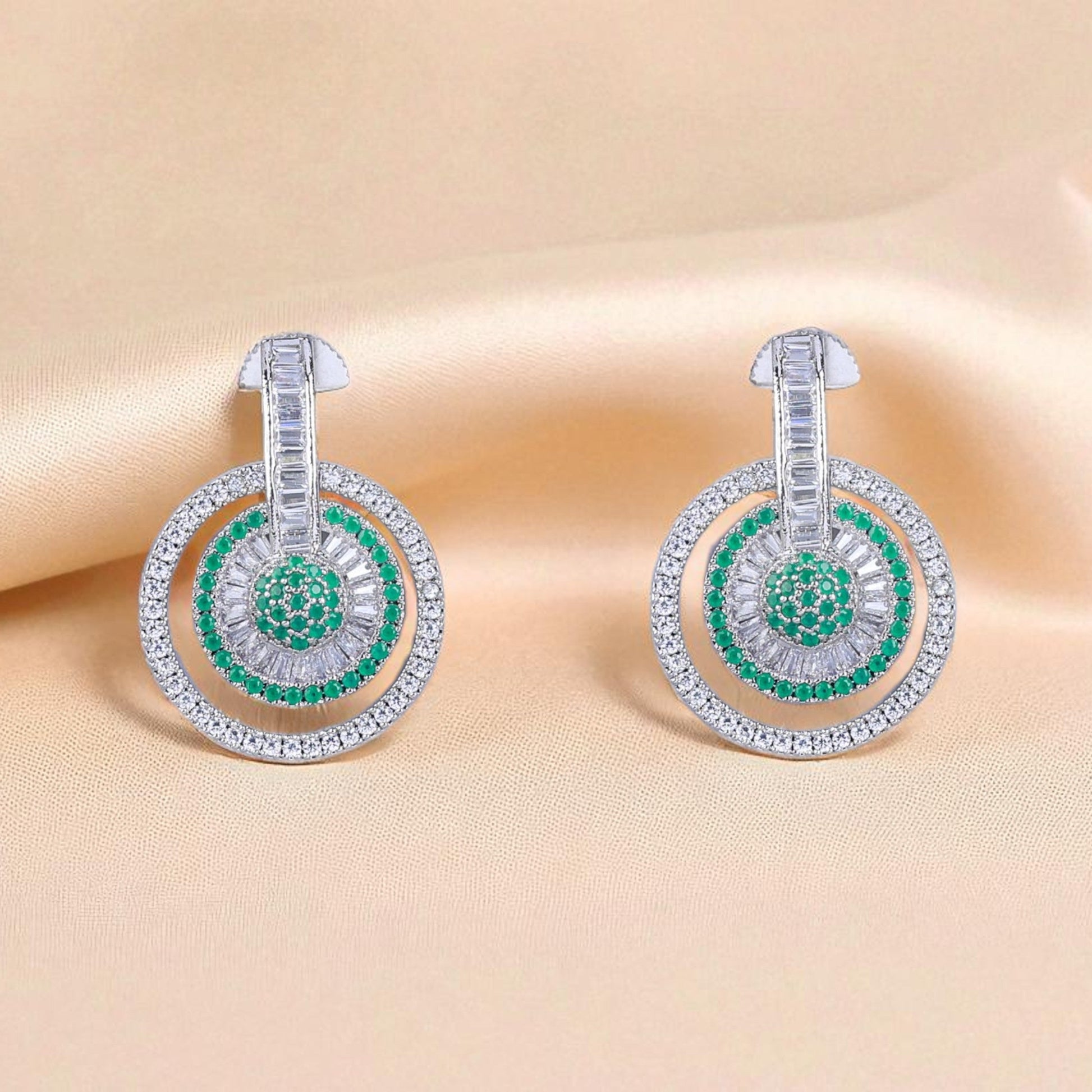 Pair of earrings with green gemstones on a beige fabric background