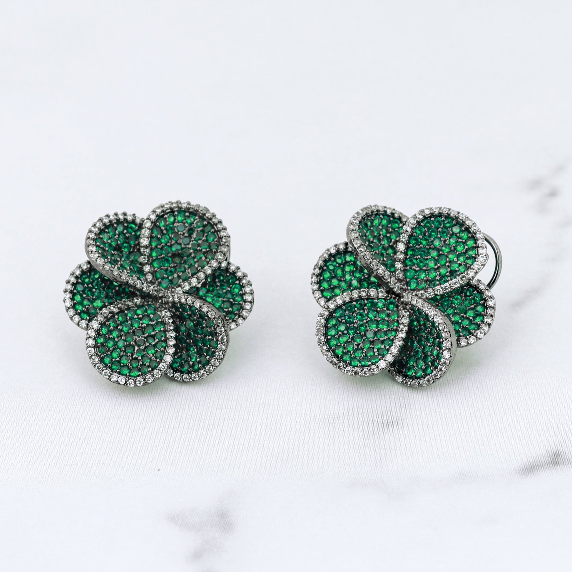 Pair of green diamond clover-shaped earrings on a marble surface
