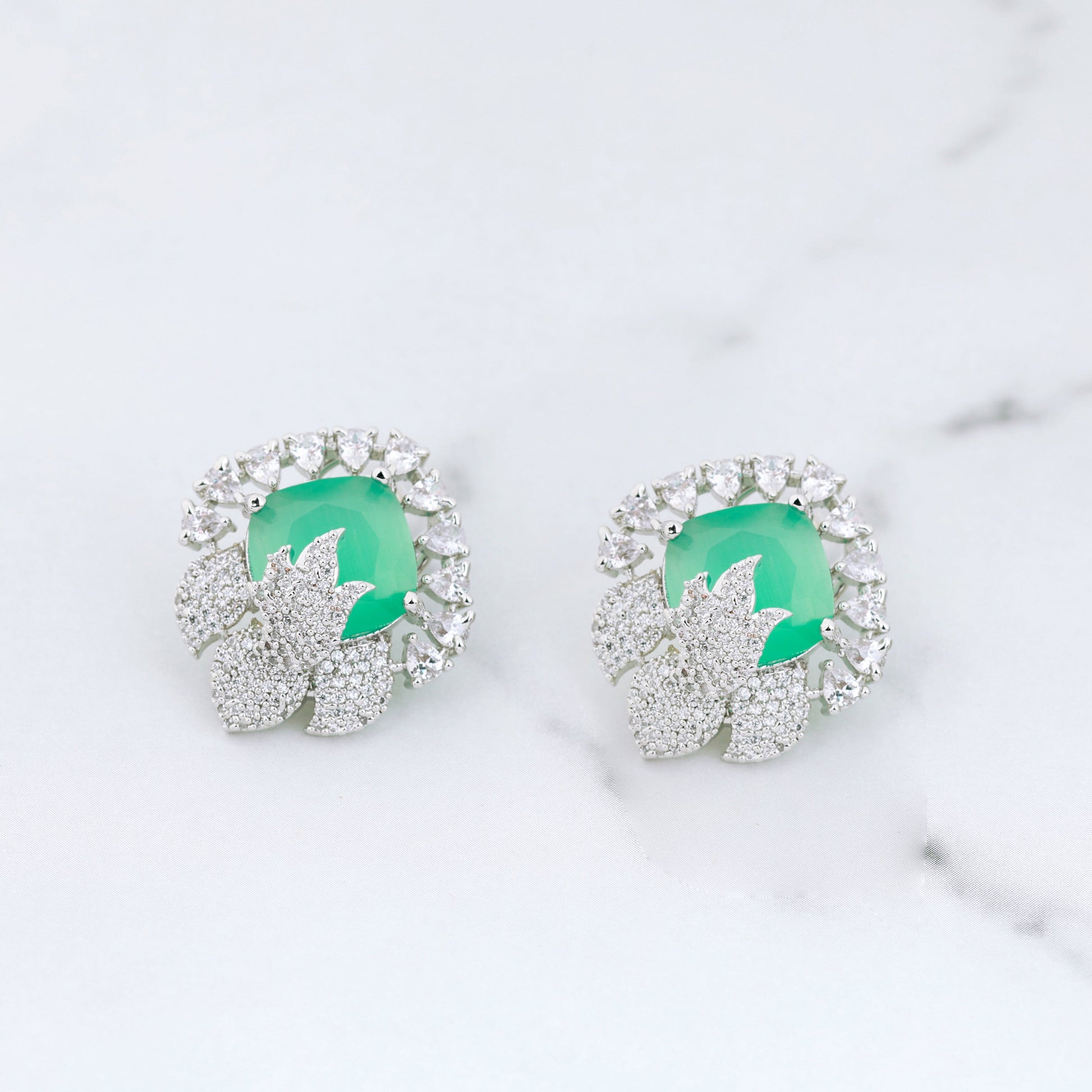 Pair of earrings with green gemstones on a marble surface