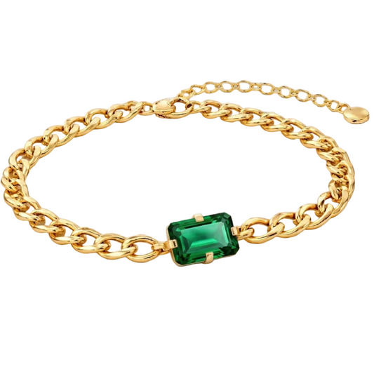 Gold chain bracelet with a green gemstone on a light gray background