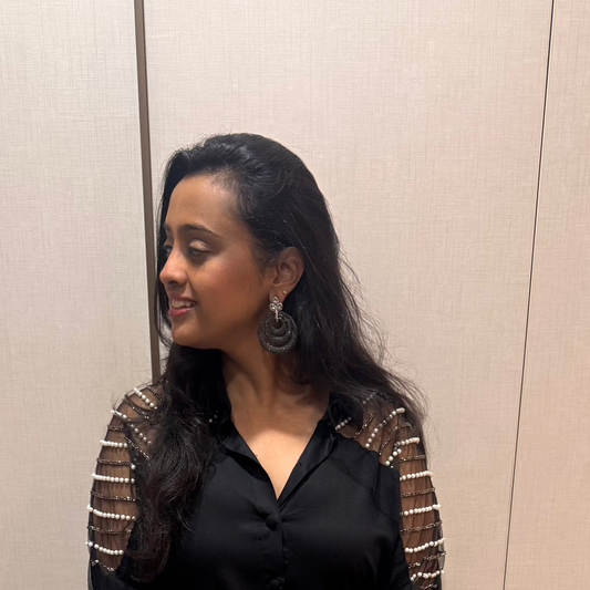 Woman in a black outfit with gold accents standing against a white wall.