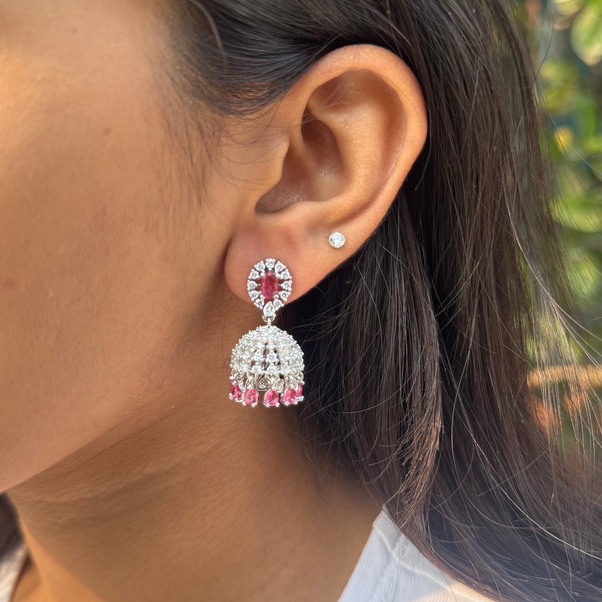 Close-up of a person wearing red and silver earrings outdoors.