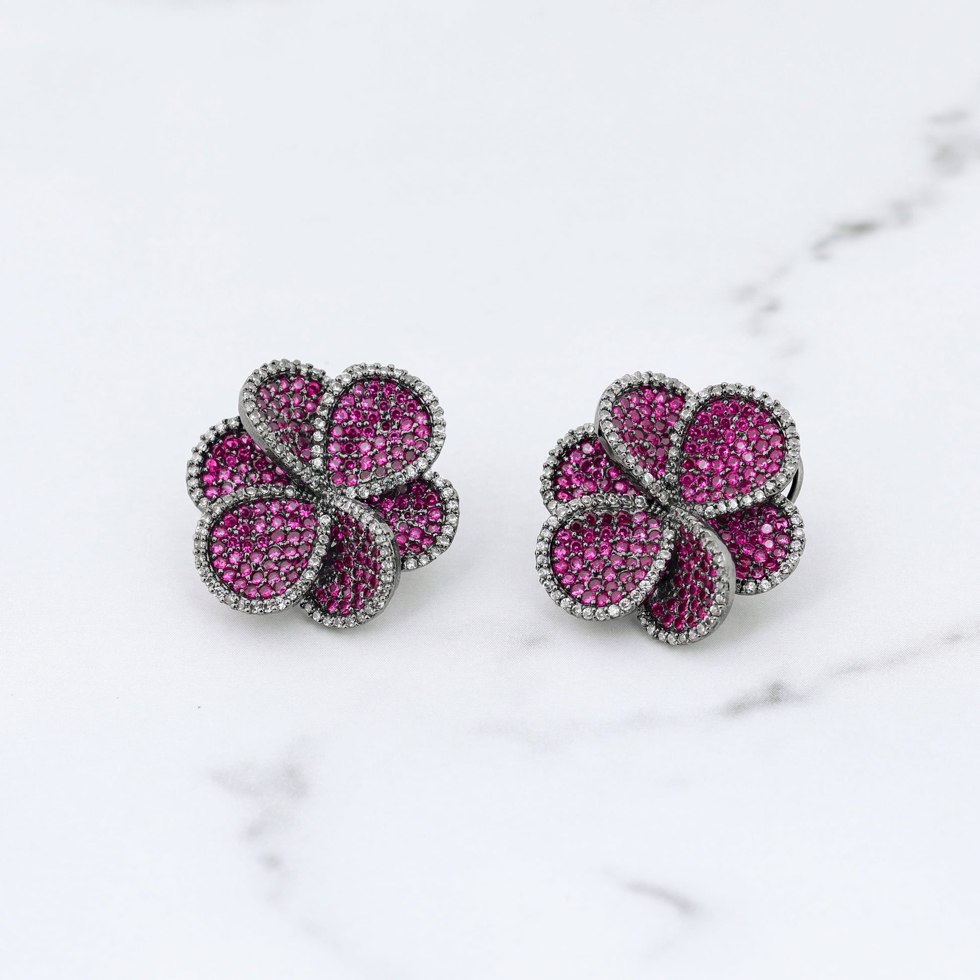 Pair of pink flower-shaped diamond earrings on a marble surface