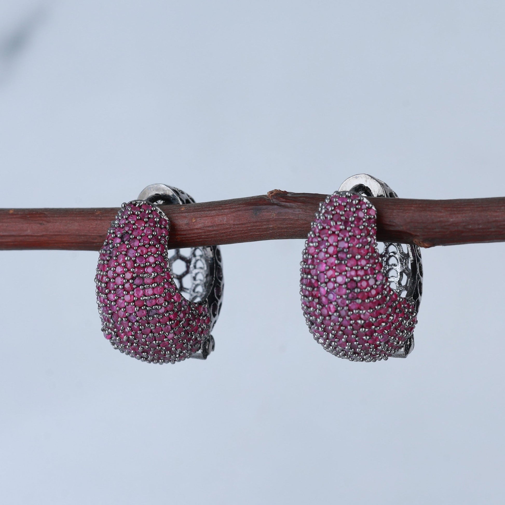 Pair of pink gemstone hoop earrings on a branch with a blurred background