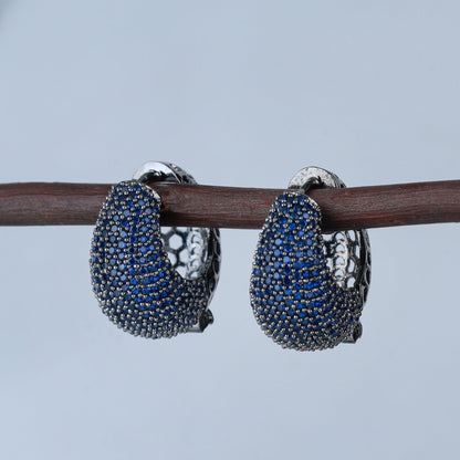 Pair of blue gemstone hoop earrings on a branch with a blurred background