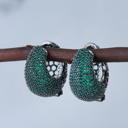 Pair of green gemstone hoop earrings on a branch with a blurred background