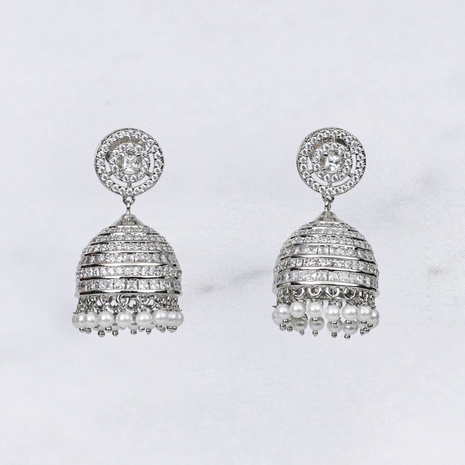 Pair of silver diamond jhumka earrings on a marble surface