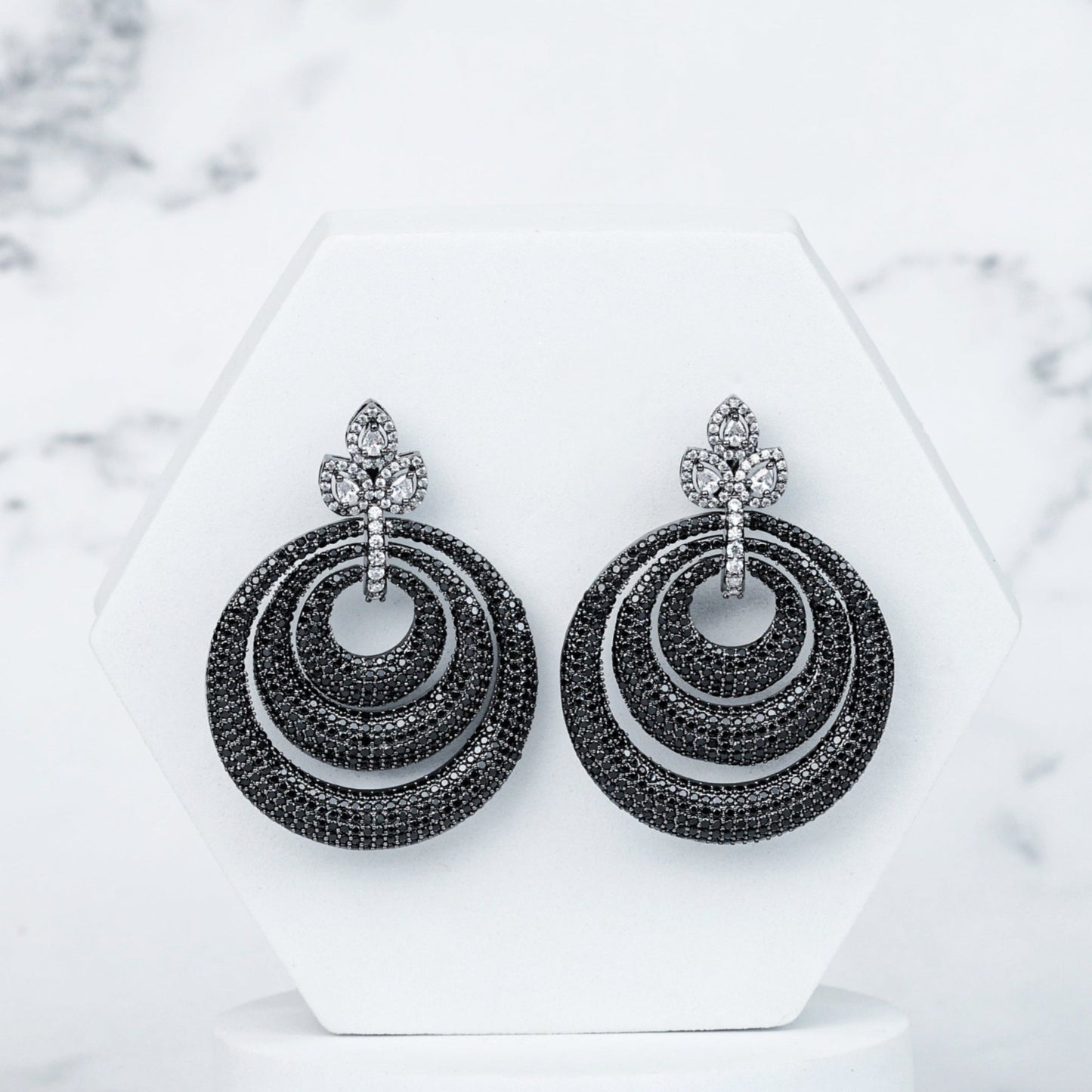 Pair of black hoop earrings on a white stand with a marble background