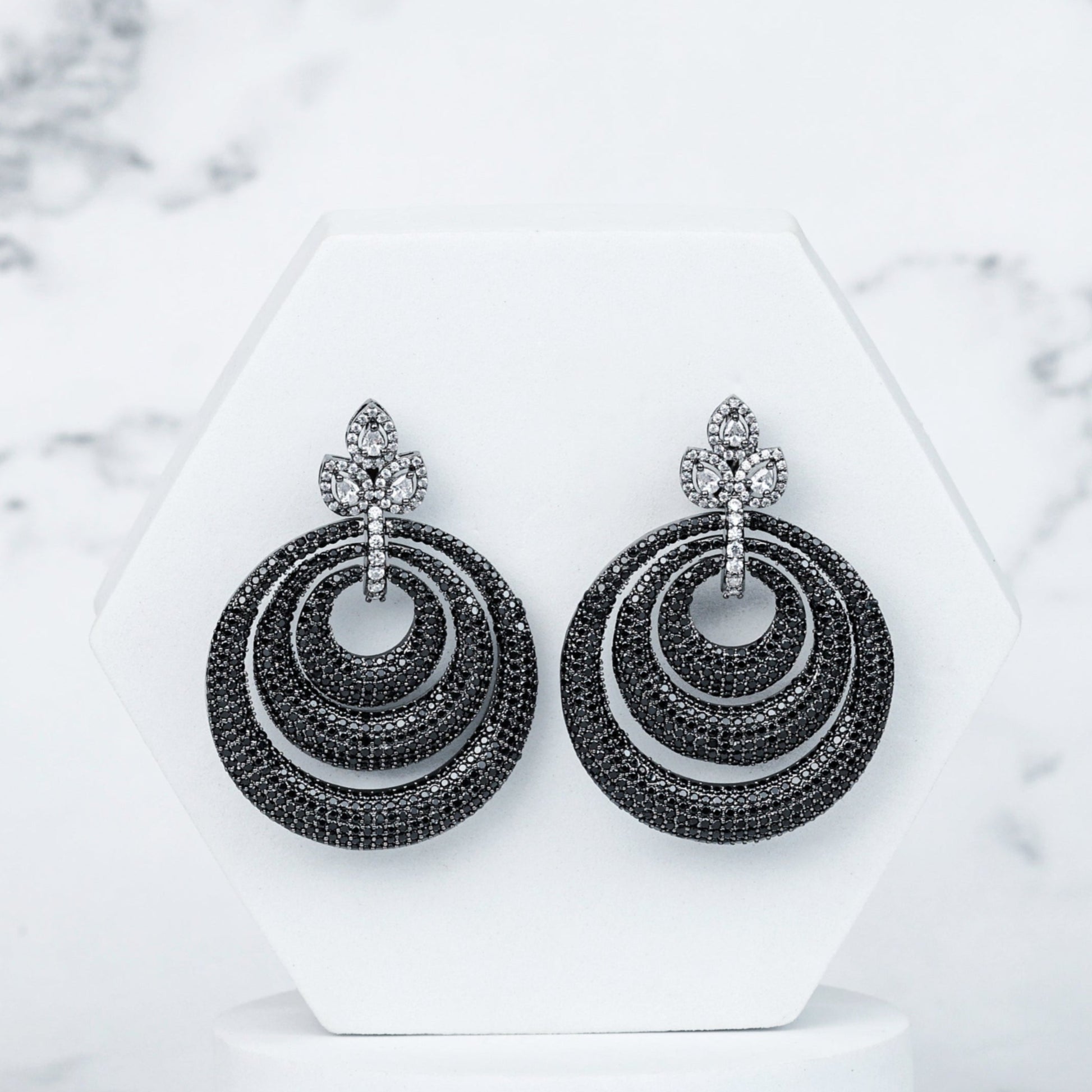 Pair of black hoop earrings on a white stand with a marble background