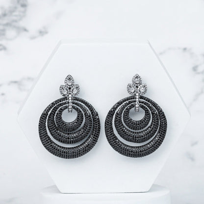 Pair of black hoop earrings on a white stand with a marble background