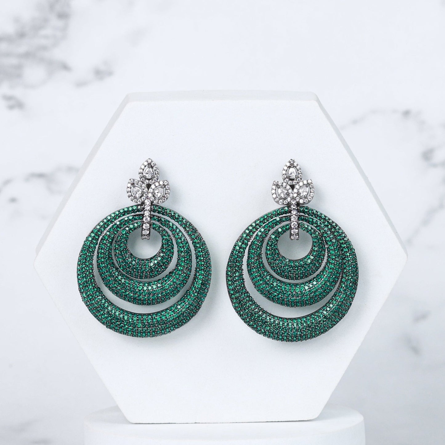 Green diamond earrings on a white stand with a marble background