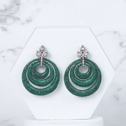 Green diamond earrings on a white stand with a marble background