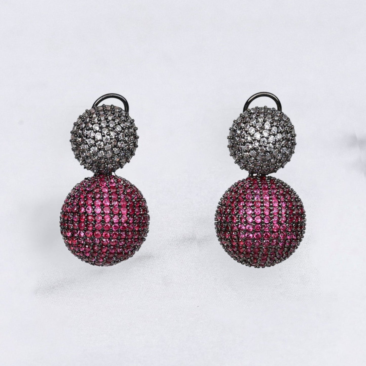 Pair of diamond earrings with pink and black spherical designs on a light gray background