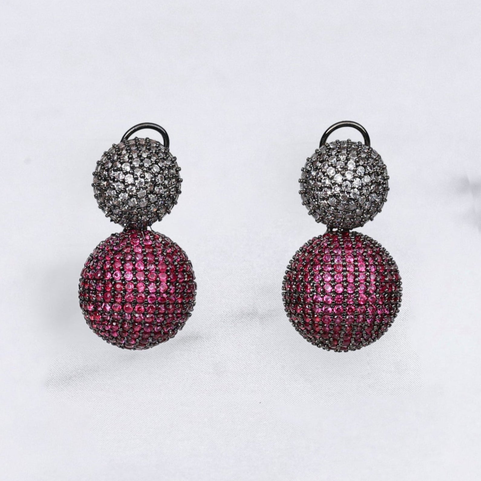 Pair of diamond earrings with pink and black spherical designs on a light gray background