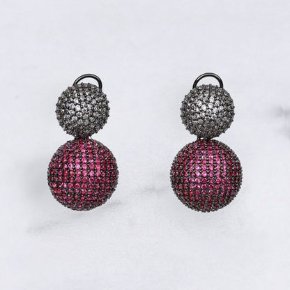 Pair of diamond earrings with pink and black spherical designs on a light gray background