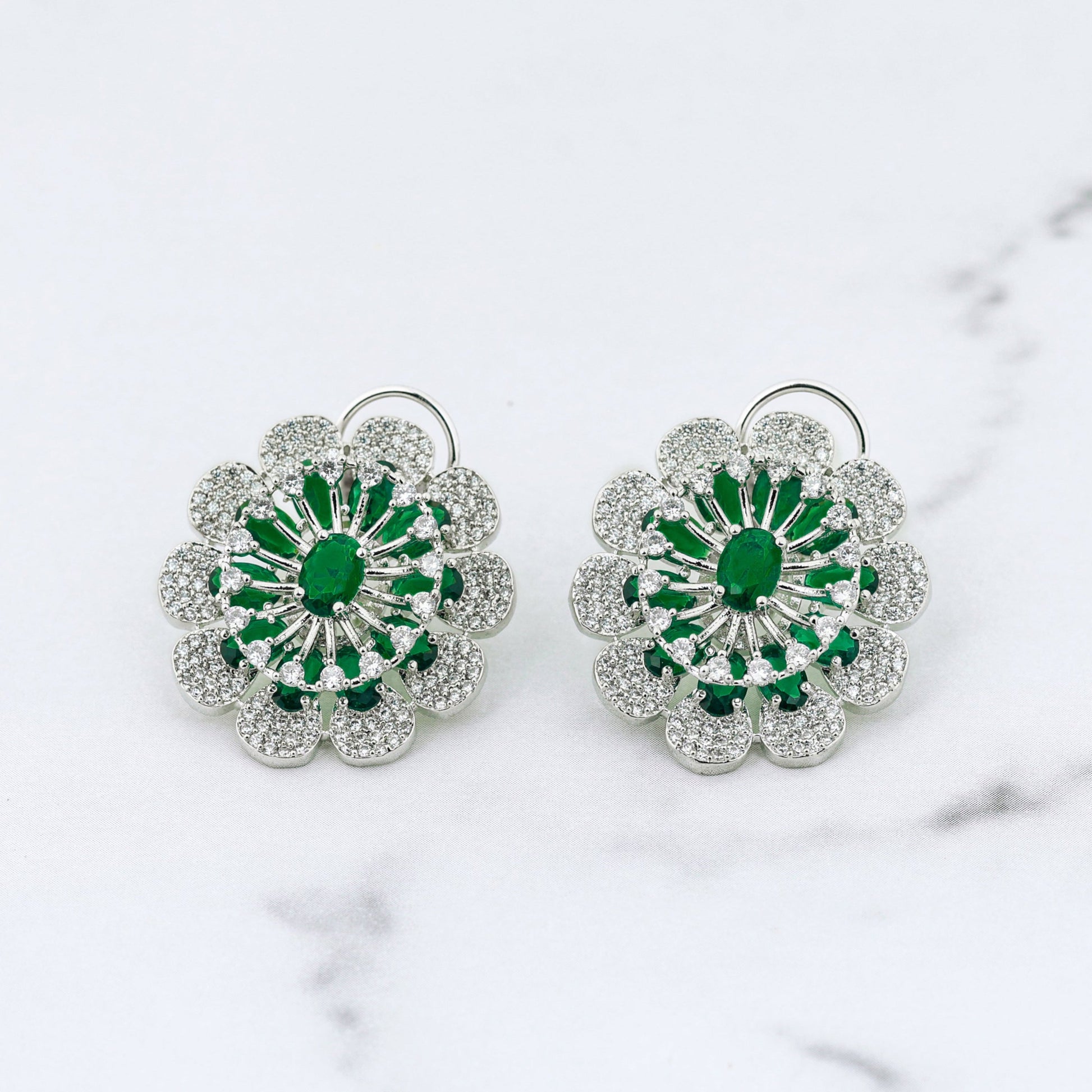 Pair of floral diamond earrings with green centers on a marble surface