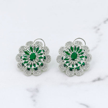 Pair of floral diamond earrings with green centers on a marble surface
