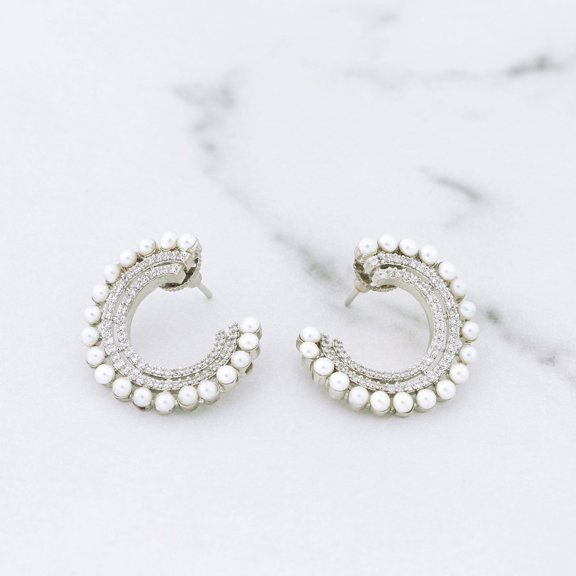 Silver hoop diamond earrings with pearl accents on a marble surface