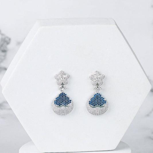 Pair of blue diamond earrings on a white hexagonal stand against a marble background