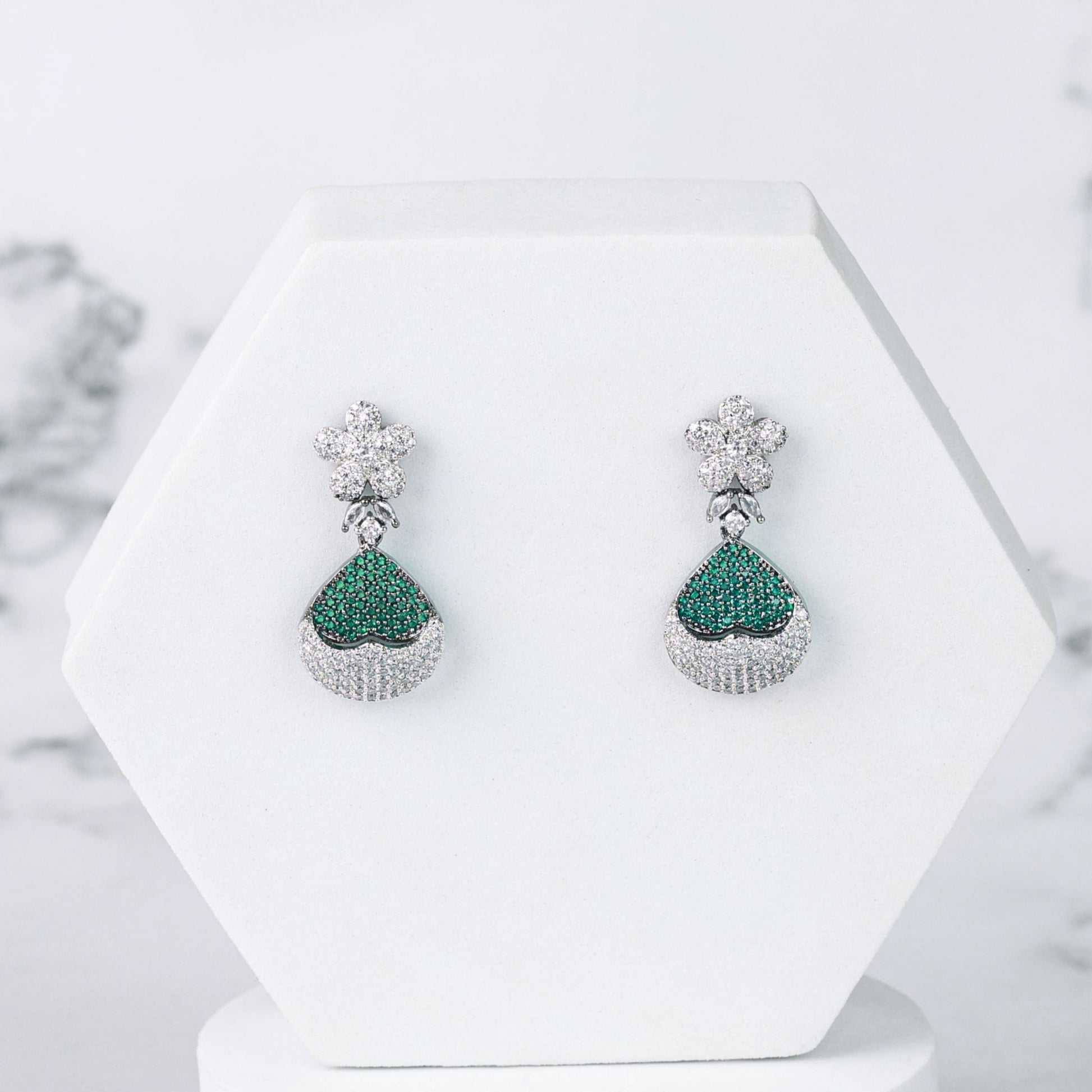 Pair of green diamond earrings on a white stand with a marble background
