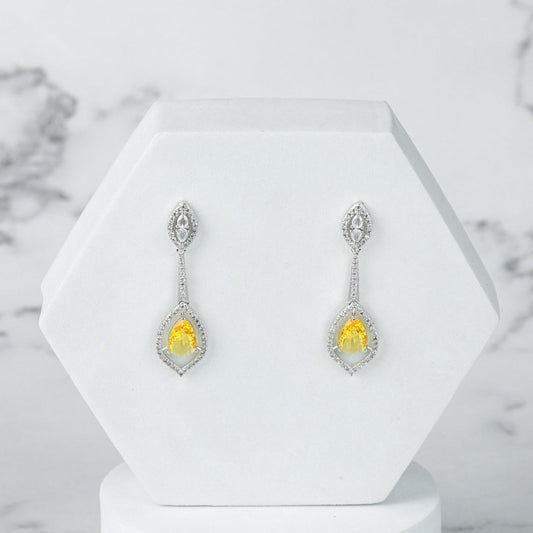 Pair of silver diamond earrings with yellow gemstones on a white stand against a marble background